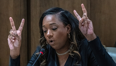 A Black woman with long hair raises her right hand.