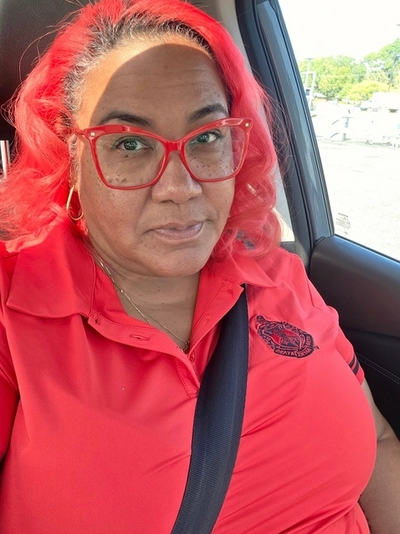 A woman in her car with her seat belt on looks at the camera.
