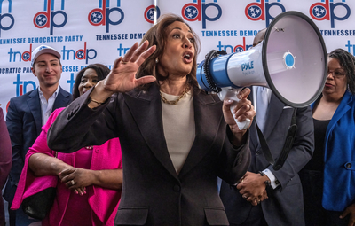 An animated, light-skinned Black woman gestures with her right hand as she speaks into a bullhorn.