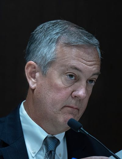 A man with gray hair and a long face looks serious.