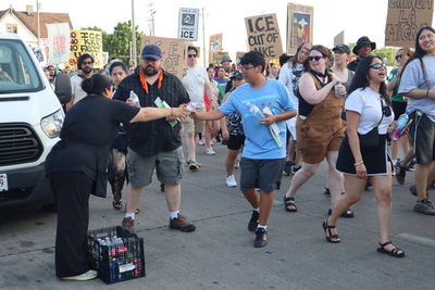A restaurant worker hands out free drinks to protesters marching in extreme heat following a surge in ICE arrests. (Photo by Isiah Holmes/Wisconsin Examiner)