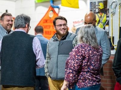 A group of people are having a conversation in an indoor setting with safety equipment and signage in the background.