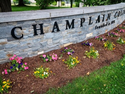 Stone wall with "Champlain College founded in 1878" written on it, bordered by a flower bed and green grass.