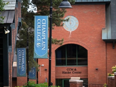 Champlain College banners hang near a brick building labeled "CCM & Hauke Center" with a clock above the entrance.