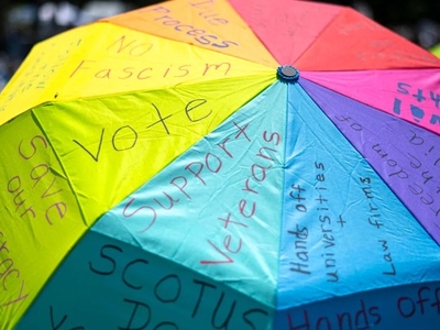A colorful umbrella with handwritten messages such as "Vote," "Support Veterans," "No Fascism," and "Save our planet" displayed across its panels.