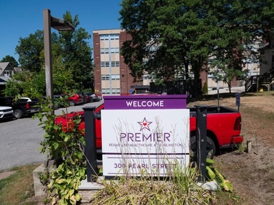 A sign reading "Premier Rehabilitation & Healthcare at Arlington, 301 Pearl Street" stands in front of a red truck and a brick building.