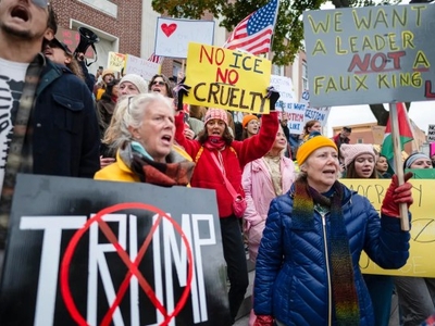 A group of protesters hold signs and shout slogans at a rally; signs include messages against Trump and calls for leadership change.