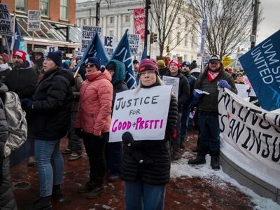 A group of people protests outdoors in winter clothing. One person holds a sign reading "Justice for Good+Pretty." Snow covers parts of the ground.