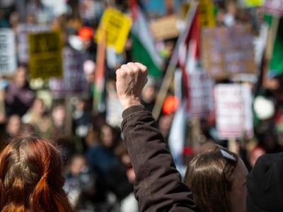 A crowd of protesters holds signs, with one person in the foreground raising a clenched fist.