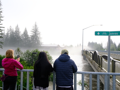 Onlookers view the glacial outburst flooding event at the Brotherhood Bridge around 8:15 a.m., just after the peak flood levels, on Aug 13, 2025 (Photo by Corinne Smith/Alaska Beacon)