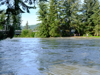 People seen on the banks of the fast-moving and flooded Mendenhall River a few hours after the peak of the glacial flooding event on Aug 13, 2025 (Photo by Corinne Smith/Alaska Beacon)