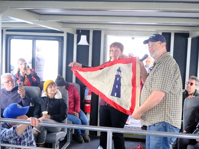 Siblings Tainya and Doug Adamson present their great-grandfather, Nils P. Adamson's flag as the first lighthouse keeper of Eldred Rock beginning in 1905 as a gift to the future maritime museum at the lighthouse on May 30, 2026. (Photo by Corinne Smith/Alaska Beacon)