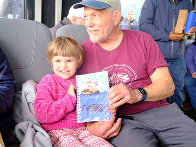 Imogene Nowlin, age 4, shows off her drawing with her grandfather Ed Page, a member of the Eldred Rock Lighthouse Preservation Association board and founder of the non-profit Marine Exchange. She spent time drawing the lighthouse on the M/V Seawolf as a smaller group of supporters disembarked on the island for the opening ceremony on May 30, 2026. (Photo by Corinne Smith/Alaska Beacon)