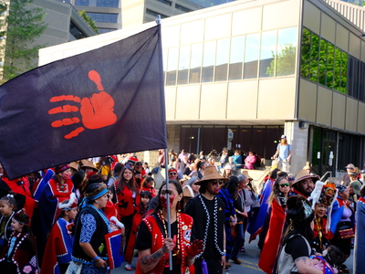 S’eiltin Jamiann Hasselquist of Juneau walks the Grand Entrance of Celebration with her face painted and carrying a flag to raise awareness for Missing and Murdered Indigenous People on June 3, 2026. (Photo by Corinne Smith/Alaska Beacon)