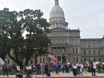 A woman holds an upside down American flag that reads 'SOS' in front of the Michigan State Capitol.