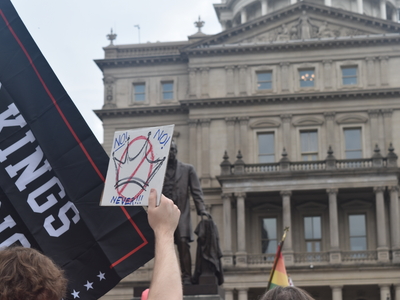A man holds a sign with a crown crossed out that reads 'No! No! Never!!'