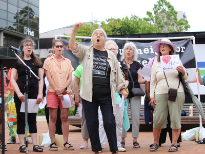 A member of the World House Choir from Yellow Springs, Ohio leads people in song at a rally for Haitians in Springfield, Ohio on June 25, 2026. (Photo by Megan Henry, Ohio Capital Journal).