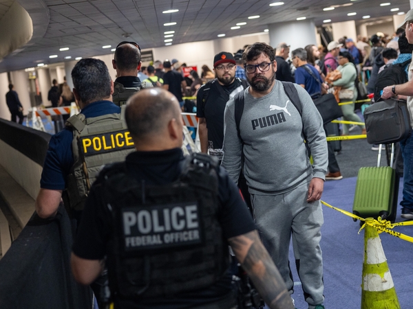 A traveler looks at Immigration and Customs Enforcement (I.C.E.) agents as they walk around the end of the line at Terminal E at George Bush Intercontinental Airport on March 24, 2026 in Houston, Texas. The travel disruptions continue as hundreds of TSA agents quit or work without pay during a partial government shutdown. U.S. President Donald Trump said ICE agents will be deployed to U.S. airports on Monday, with border czar Tom Homan in charge of the effort. (Photo by Antranik Tavitian/Getty Images)