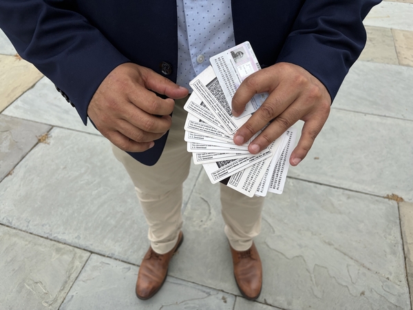 Jose Palma holds the work authorization cards of a Salvadoran member of the National TPS Alliance. The individual has renewed work permits 14 times since TPS was granted for El Salvador in 2001, submitting a background check and fingerprints with each renewal cycle. (Photo by Ariana Figueroa/States Newsroom)