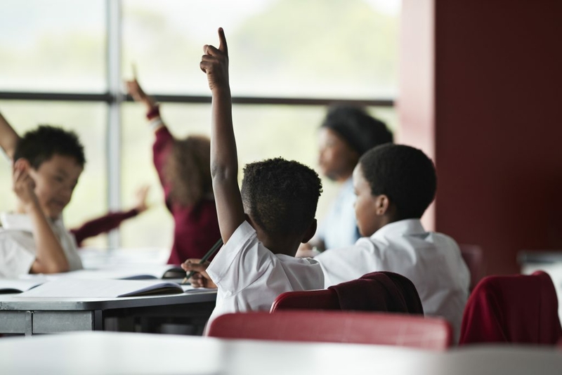 Children raising their hands in a classroom/Getty Images