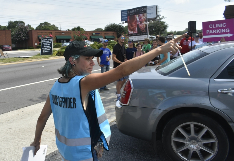 Abortions rights activist Kristin Hadyl points a car past protesters toward the health center. Ross Williams/Georgia Recorder.