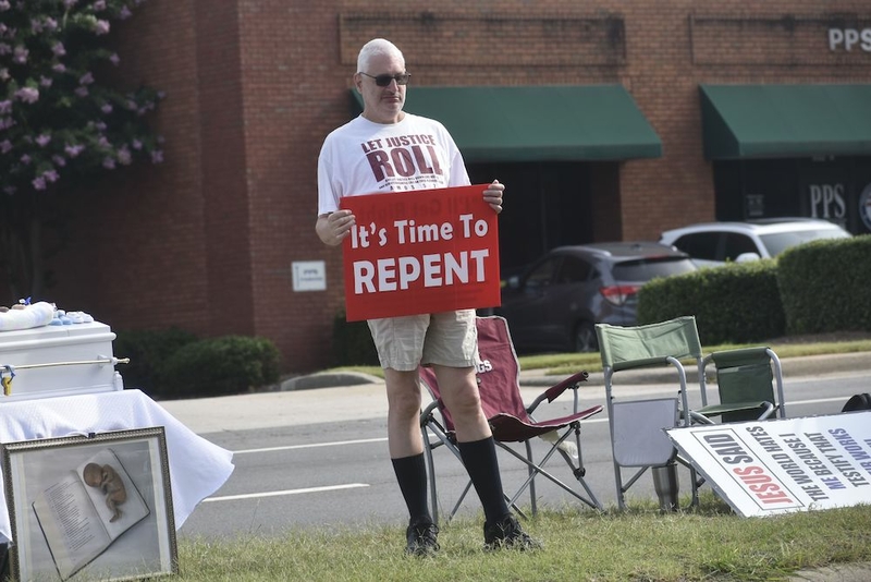 Abortion protester stands in the grassy median outside A Preferred Women’s Health Care Center of Atlanta in Forest Park. (Ross Williams/Georgia Recorder)