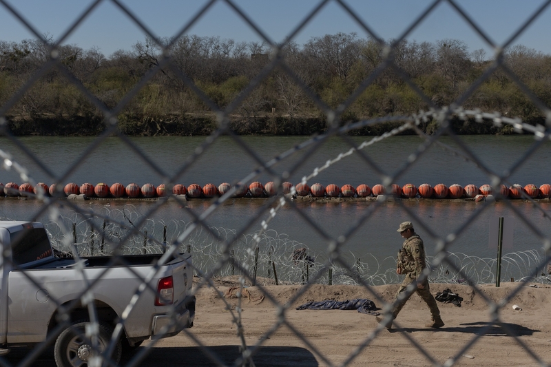 A Texas National Guard member walks past a line of buoys in Eagle Pass, on Jan. 17, 2024. (Photo by Eddie Gaspar / The Texas Tribune)