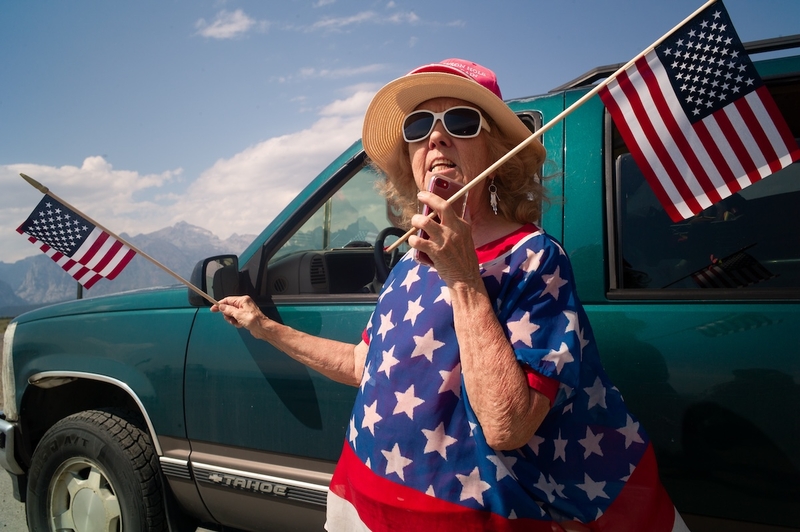 With the Grand Teton looming behind her, Margie Aeckerle waits by the highway hoping to get a glimpse of former President Donald Trump during his fundraising visit to Jackson Hole. (Angus M. Thuermer Jr./WyoFile)