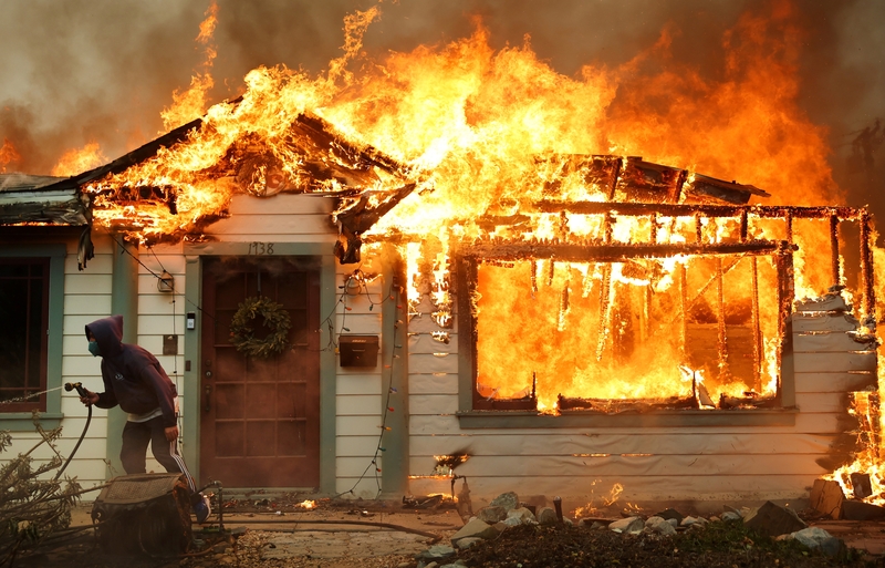A person uses a garden hose in an effort to save a neighboring home from catching fire during the Eaton Fire on Jan. 8, 2025 in Altadena, California. (Photo by Mario Tama/Getty Images)