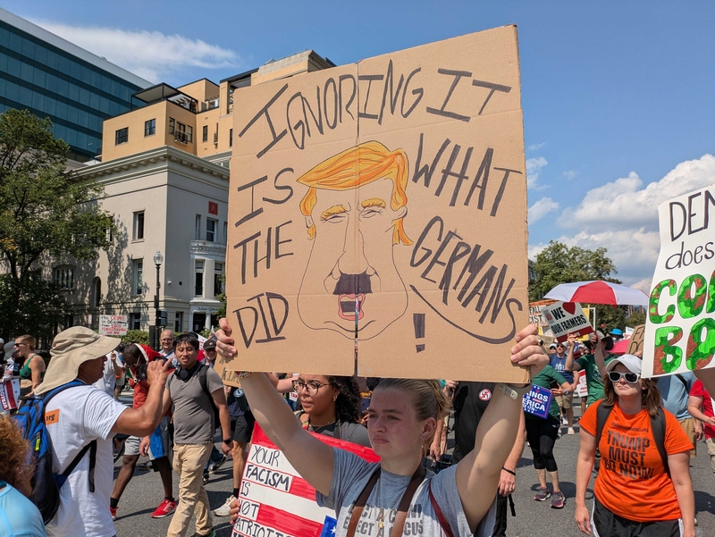 Charlotte Stone, 18, of Virginia Beach, Virginia, held a sign depicting President Donald Trump with a Hitler mustache, at the "We Are All DC" march Saturday, Sept. 6, 2025, in the District of Columbia to protest the deployment of National Guard troops in the nation's capital. (Photo by Ashley Murray/States Newsroom)