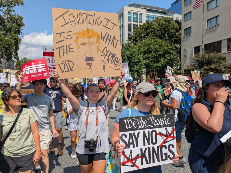 Charlotte Stone, 18, of Virginia Beach, Virginia, held a sign depicting President Donald Trump with a Hitler mustache, at the "We Are All DC" march Saturday, Sept. 6, 2025, in the District of Columbia to protest the deployment of National Guard troops in the nation's capital. (Photo by Ashley Murray/States Newsroom)