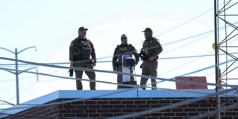 Three men in Customs and Border Protection uniforms stand on the roof of the Broadview immigration facility taking pictures of the surrounding area on Oct. 9. (Capitol News Illinois photo by Andrew Adams)