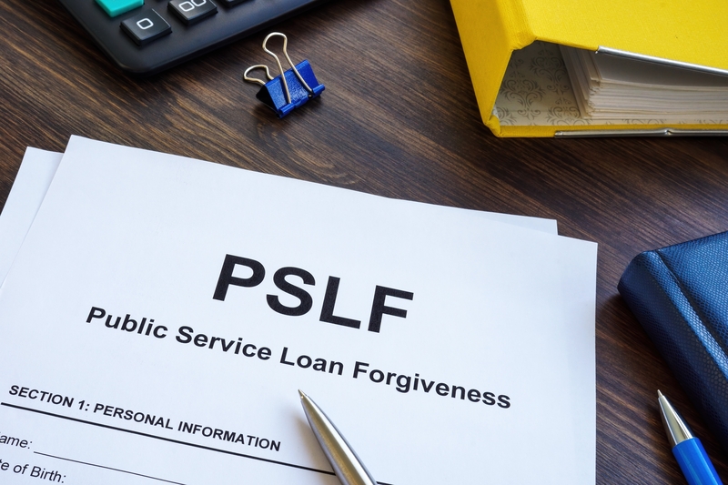 Forms with "Public Service Loan Forgiveness" printed at the top sit on a desk alongside other common desk items.
