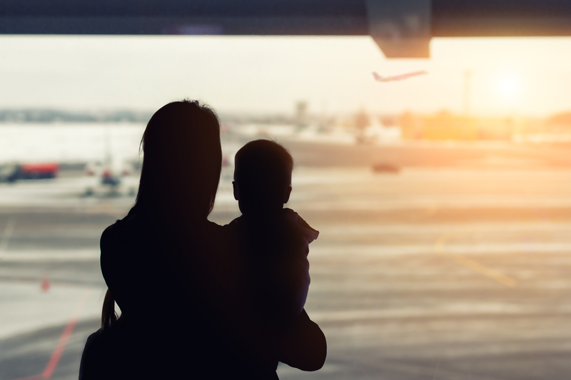 A woman holds a baby as they look out an observation window at an airport to see the planes.