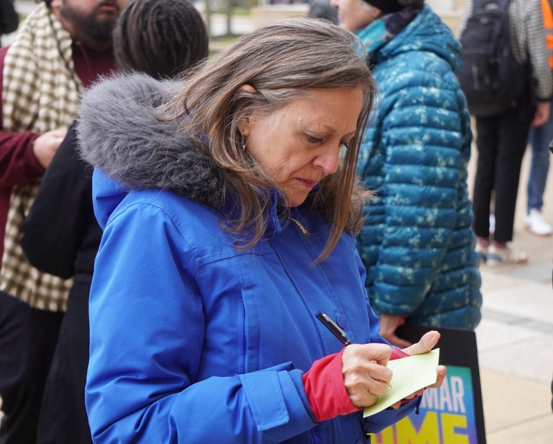 After a rally outside the U.S. District Court in Greenbelt, Maryland, on Nov. 20, 2025, Jacki Gilbert of Baltimore writes on a postcard to be delivered to Kilmar Abrego Garcia. (Photo by William J. Ford/Maryland Matters)