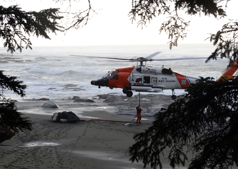 Petty Officer 3rd Class Michael Tate, an aviation maintenance technician at Coast Guard Air Station Astoria, hooks up a net full of beach debris and trash to the bottom of an MH-60 Jayhawk helicopter at a beach near Neah Bay, Wash., Jan. 22, 2015. (Photo by U.S. Coast Guard Petty Officer 3rd Class Jonathan Klingenberg)
