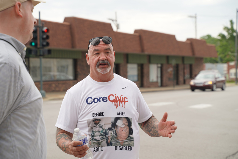 William Rogers stands holding a water bottle wearing a graphic shirt with images of injuries sustained by corrections officers while employed by CoreCivic.