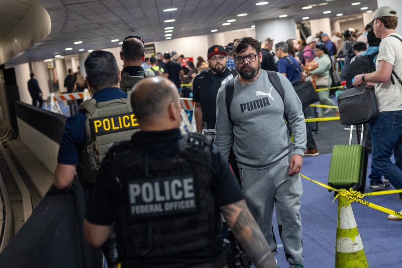 A traveler looks at Immigration and Customs Enforcement agents as they walk around the end of the line at Terminal E at George Bush Intercontinental Airport on March 24, 2026 in Houston, Texas. Travel disruptions continue as hundreds of TSA agents quit or work without pay during a partial government shutdown and ICE agents are sent to some airports to assist. (Photo by Antranik Tavitian/Ge
