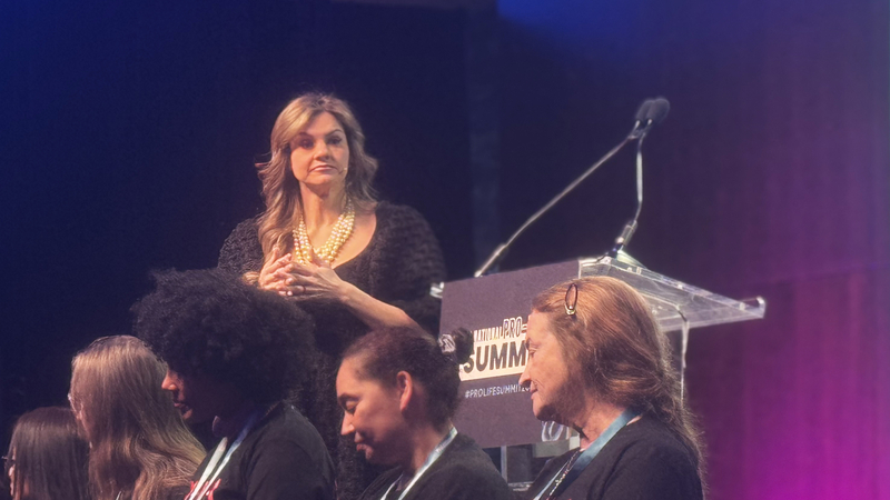 Anti-abortion organizer Abby Johnson spoke at Students for Life of America’s annual National Pro-Life Summit on Jan. 24, 2026, behind former abortion clinic workers wearing “Make Abortion Murder Again” T-shirts. “I don’t think we’re going to hug and kiss our way out of this baby murder,” she told the student activists. (Photo by Sofia Resnick/States Newsroom)
