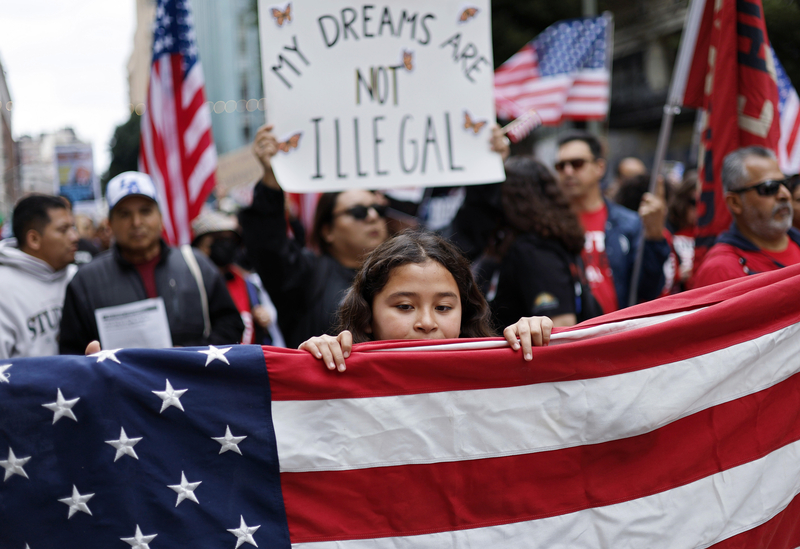 LOS ANGELES, CALIFORNIA - MARCH 01: A demonstrator carries a sign reading 'My Dreams Are Not Illegal' near American flags as immigrants rights supporters march downtown during a 'March for Dignity' on March 01, 2025 in Los Angeles, California. The march was organized by faith groups along with immigrants rights organizations as a peaceful protest over the Trump administration's immigration policies. (Photo by Mario Tama/Getty Images)