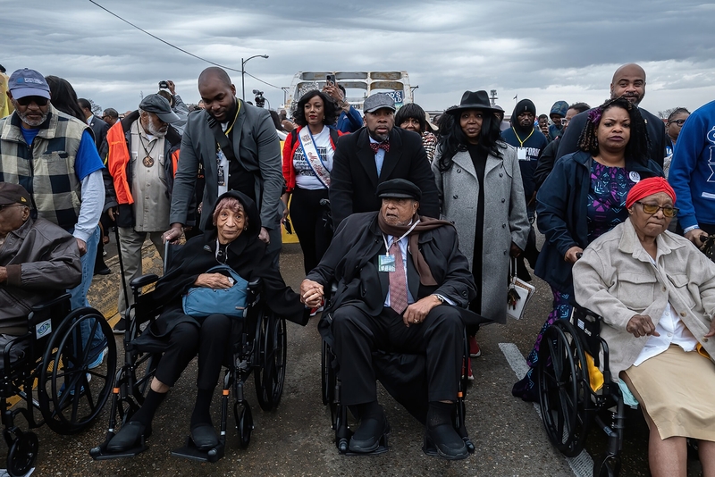 Rev. Bernard LaFayette (center, in wheelchair and cloth cap) holds his wife Kate’s hand as they are wheeled over the Edmund Pettus Bridge in Selma, Alabama on March 9, 2025 as part of 60th anniversary commemorations of Bloody Sunday, the 1965 attack on peaceful civil rights protestors that led to the Selma-to-Montgomery March and the Voting Rights Act. LaFayette ran the Selma voting rights campaign in 1965 and survived an assassination attempt. (Photo by John Partipilo/Tennessee Lookout)
