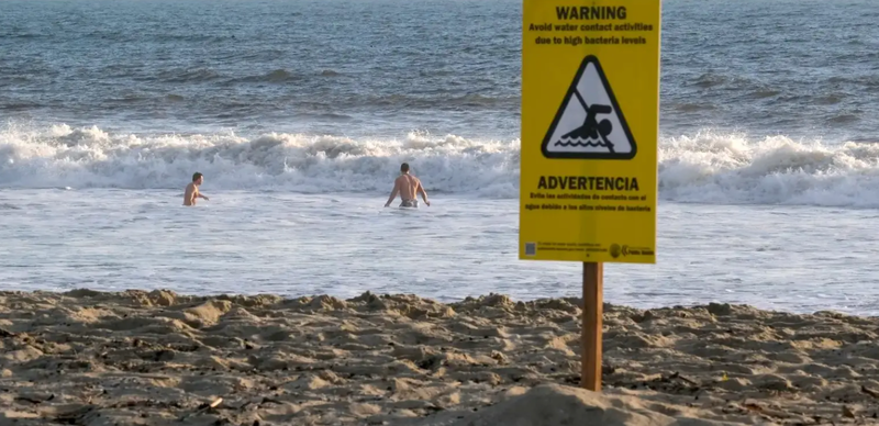 A sign warning of high bacteria levels in the water is seen on the beach as people swim in California. Chris Delmas / AFP / Getty Images via Grist