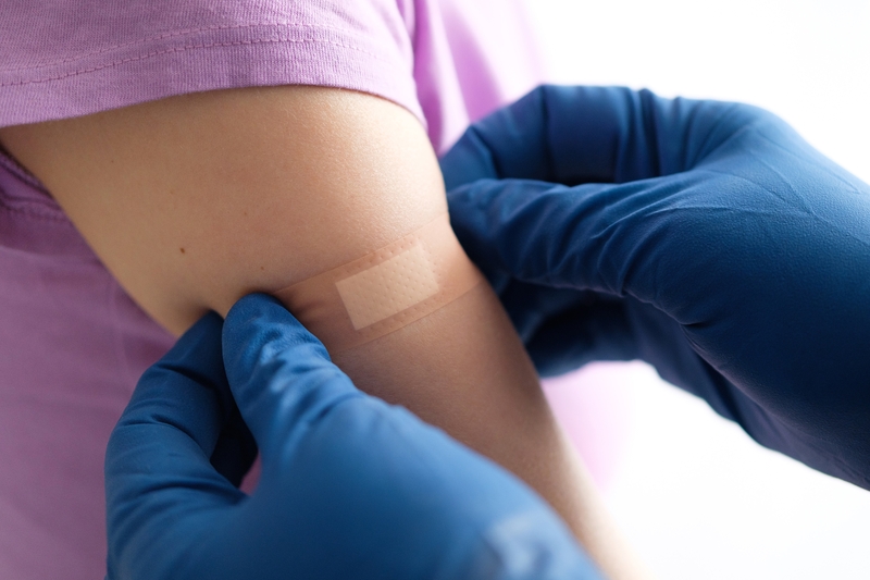 A gloved doctor or health care professional applies a patch or adhesive bandage to a girl or young woman after vaccination or drug injection.