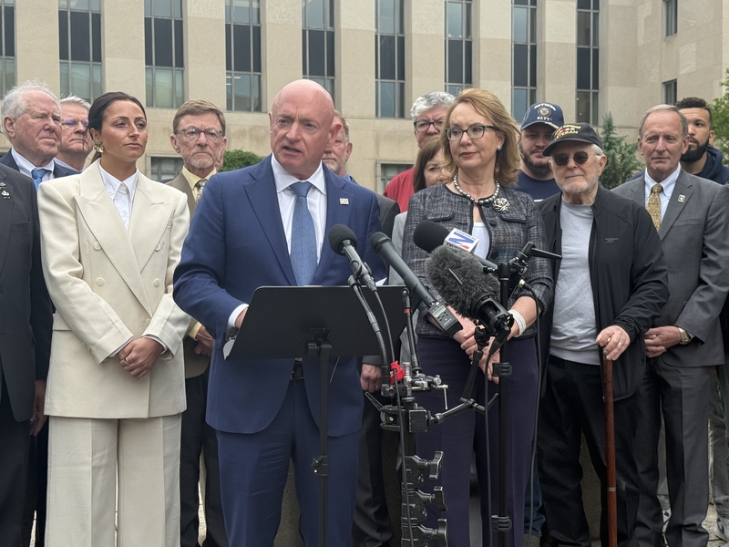 Arizona Democratic Sen. Mark Kelly speaks outside the E. Barrett Prettyman U.S. Courthouse and William B. Bryant Annex in Washington, D.C., on Thursday, May 7, 2026, following oral arguments in federal appeals court in his case against the Defense Department. Former Arizona Rep. Gabby Giffords, who is married to Kelly, and supporters surround Kelly. (Photo by Jennifer Shutt/States Newsroom)