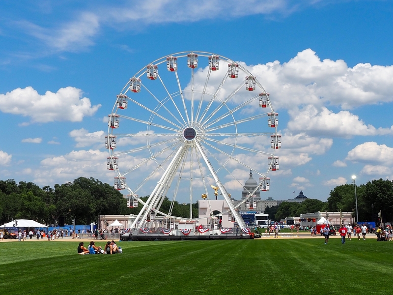 Attendees sit in the grass in front of the Ferris wheel at the Trump administration's Freedom 250 Great American State Fair on the National Mall on Thursday, June 25, 2026. (Photo by Ashley Murray/States Newsroom)