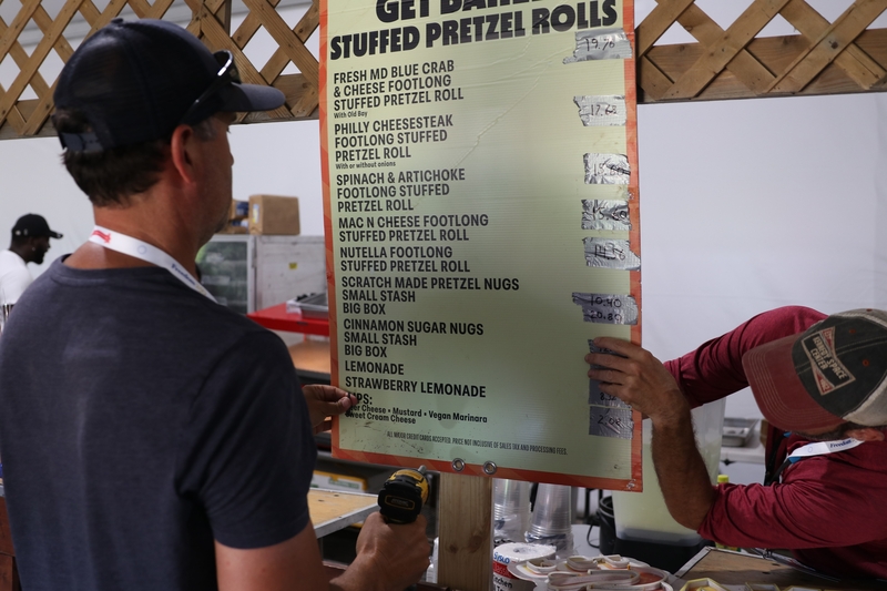 Workers hang up a menu, with drawn-on prices, in a concessions area along the National Mall ahead of the Freedom 250 kick-off celebration in Washington, D.C. on June 24, 2026. (Sam Gauntt/States Newsroom)