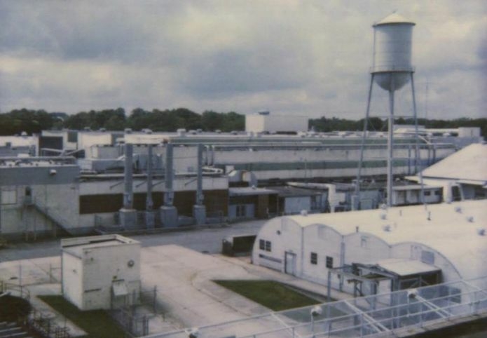 A black-and-white Polaroid of the Tarheel Army Missile Plant in Burlington in the 1990s. There is an elevated water tower, several yurts and long brick buildings, with large expanses of concrete over 22 acres.