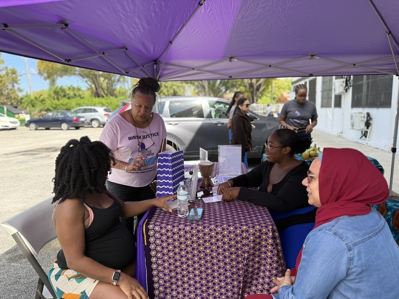 Doulas chat with patient Isis Daaga, seated left, at the mobile midwifery clinic’s booth in Miami at the Freedom Lab on March 21. (Photo by Nada Hassanein/Stateline)