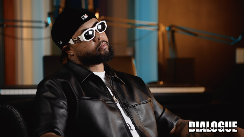 A person in white sunglasses and a black leather jacket sits in a room during an interview.