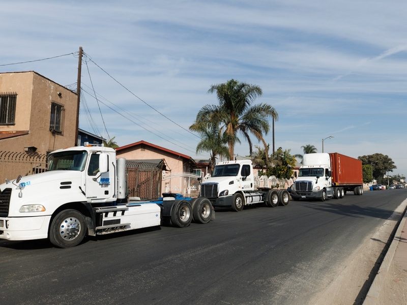 A wide-view of three commercial trucks parked on the side of a streets with houses in the background.